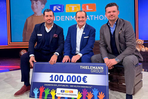 Navid Thieleman, Wolfgang Kons und Christian Flick (von links nach rechts) sitzend, davor der symbolische Scheck von 100.000 Euro