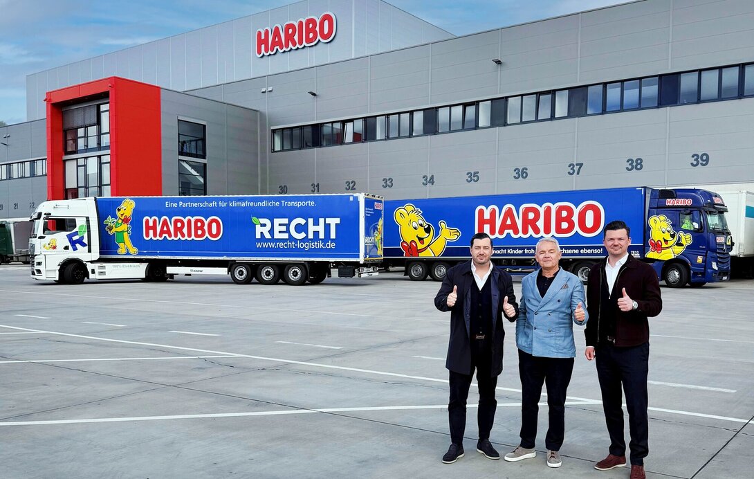 (Von links): Navid Thielemann, CEO der ThielemannGroup, Stefan Sorce, Geschäftsführer der HARIBO Logistik, sowie Christian Flick, CEO der RECHT Logistik GmbH und COO der ThielemannGroup, stehen am HARIBO-Standort Grafschaft vor dem neuen E-LKW und einem weiteren HARIBO-LKW